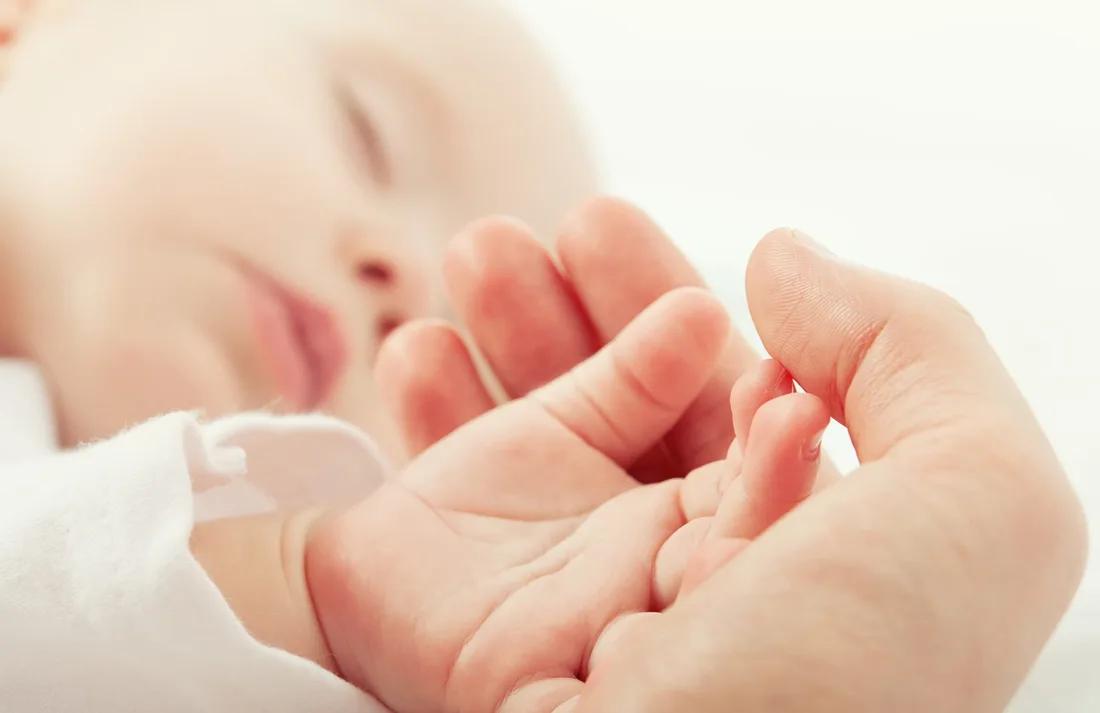 A baby’s small hand resting against a parent’s finger